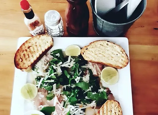 Fresh salad with shaved cheese, leafy greens, lime wedges, and toasted bread served at Kokkos Cafe Bistro in Diani Beach.