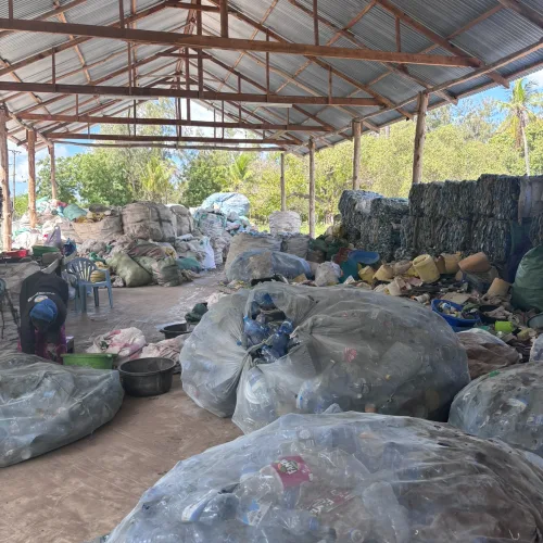 Large bags of sorted plastic bottles inside a recycling facility with workers and storage area